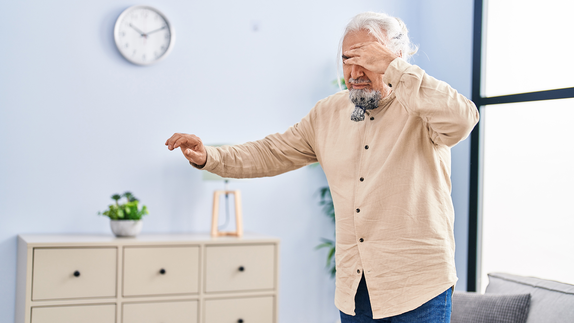 an older man is shown standing in a medical office while fighting through dizziness as he holds his hand up to his head