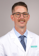 Cam Upchurch smiling and posing in a white coat