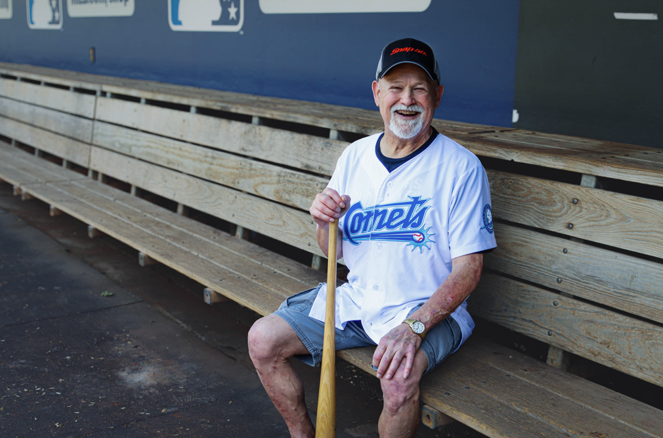 Male sitting in a dugout holding a baseball bat