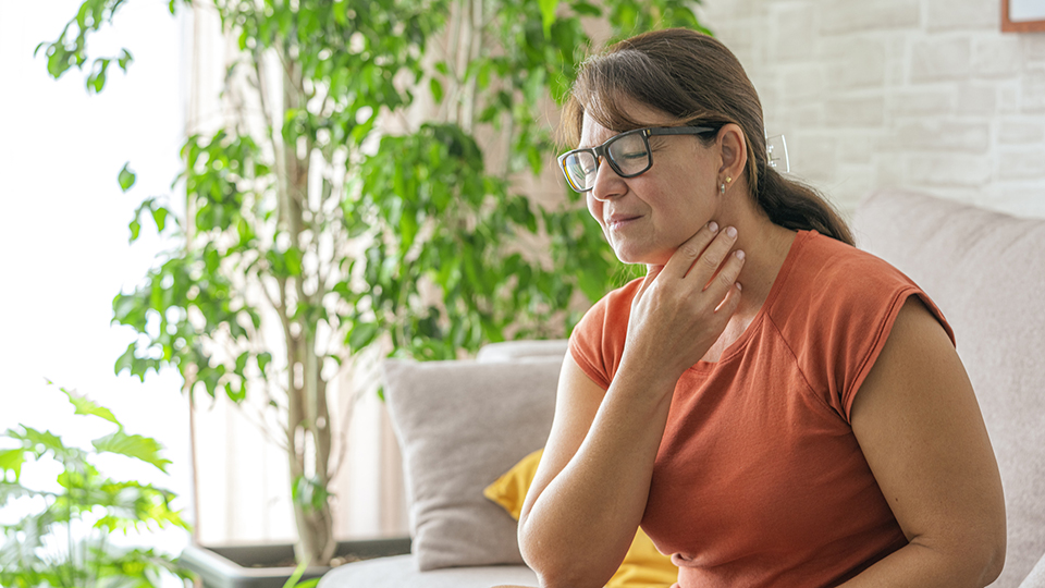 Woman sitting on sofa feeling sore throat.