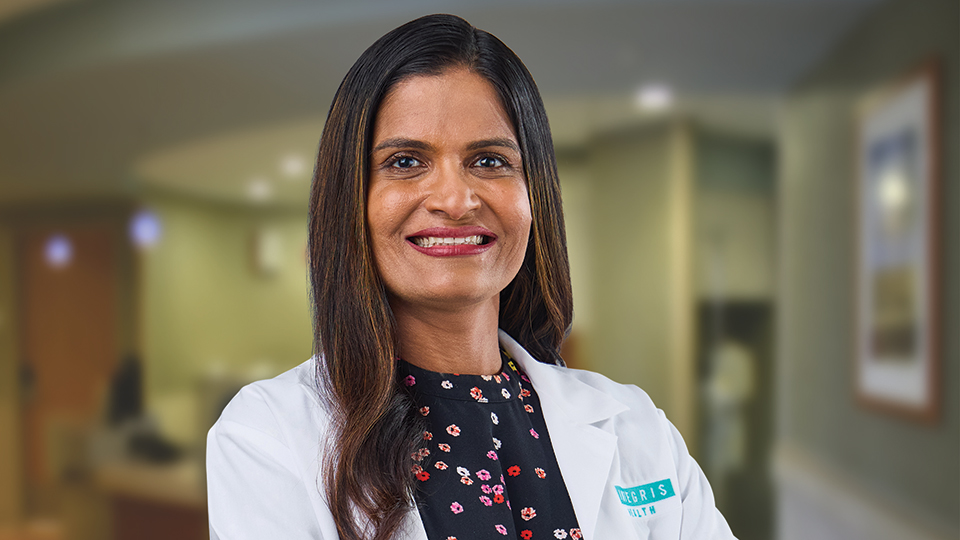 Pramoda Koduru smiling and posing in a white physician coat