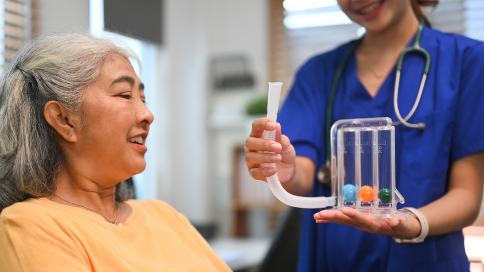 A physical therapist holding a spirometer assisting a patient to improve lung function