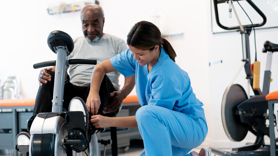 Man on a physical therapy bike receiving helping from a nurse