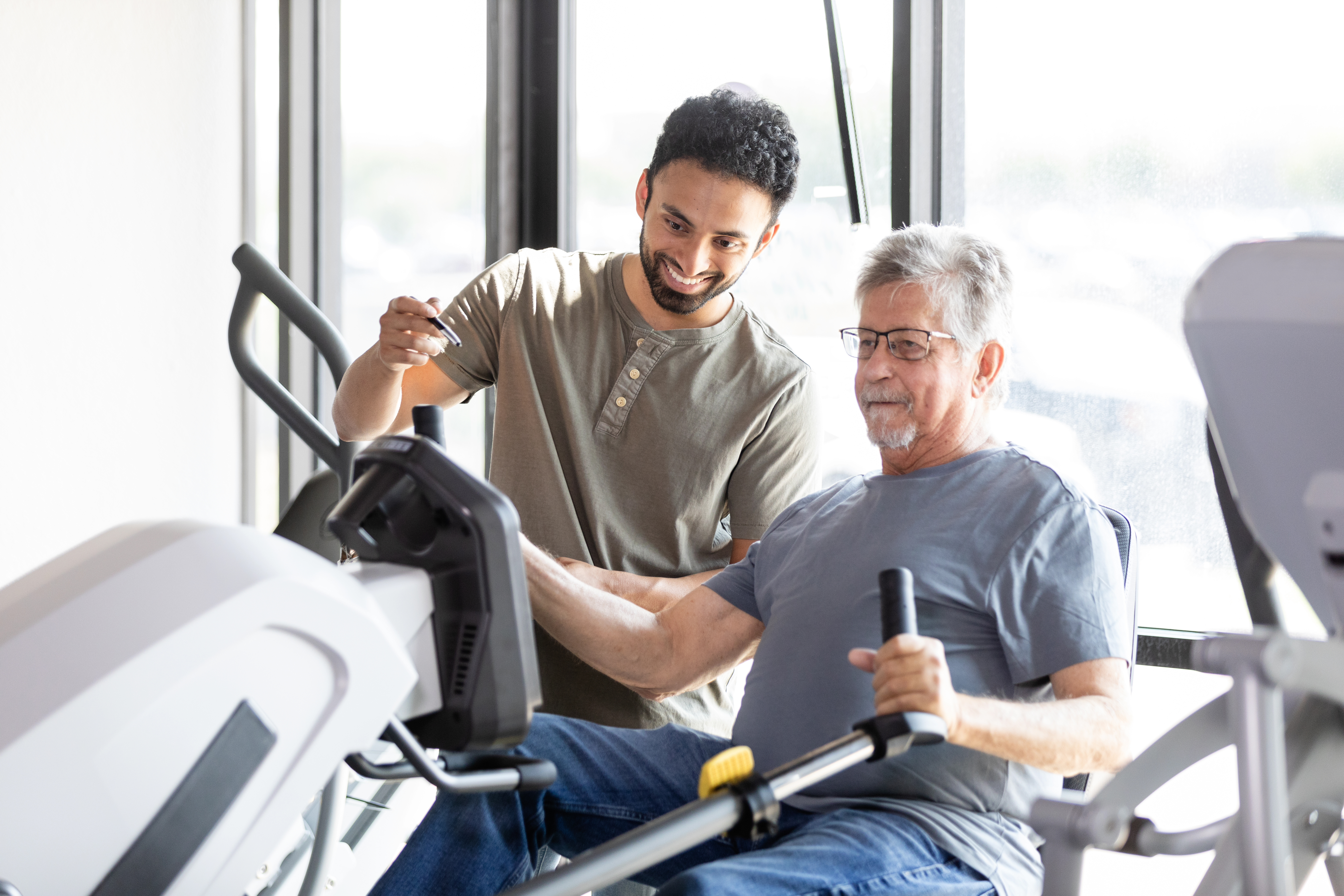 Young adult male technician smiles as he supervises his mature male patient