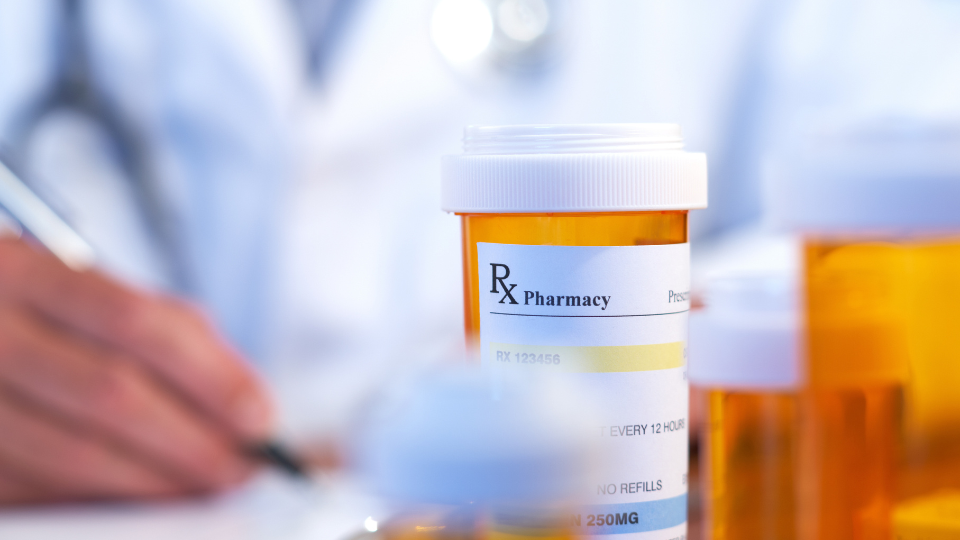 Doctor writing a prescription with Rx bottles on the table