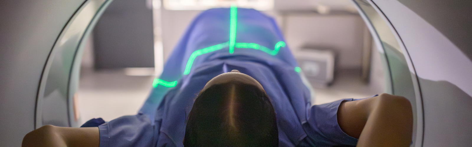 Female patient undergoing a scan lying inside a medical imaging machine with alignment lasers