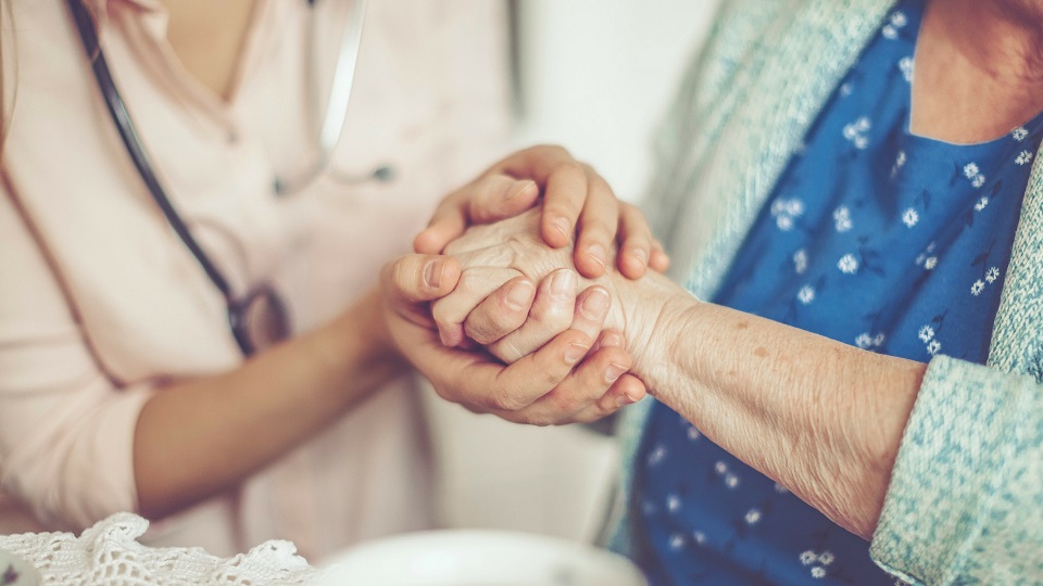 senior woman and nurse holding hands