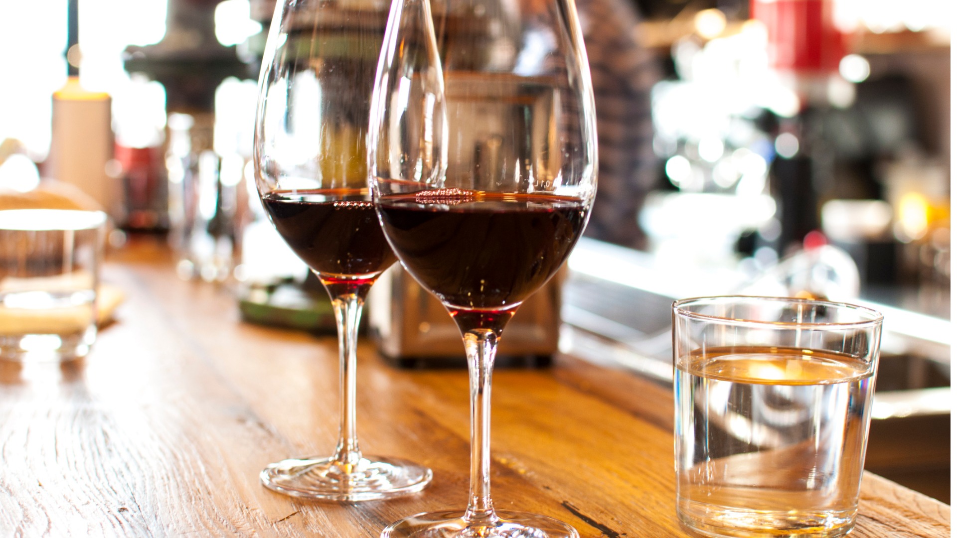 two wine glasses and a glass of water on a bar