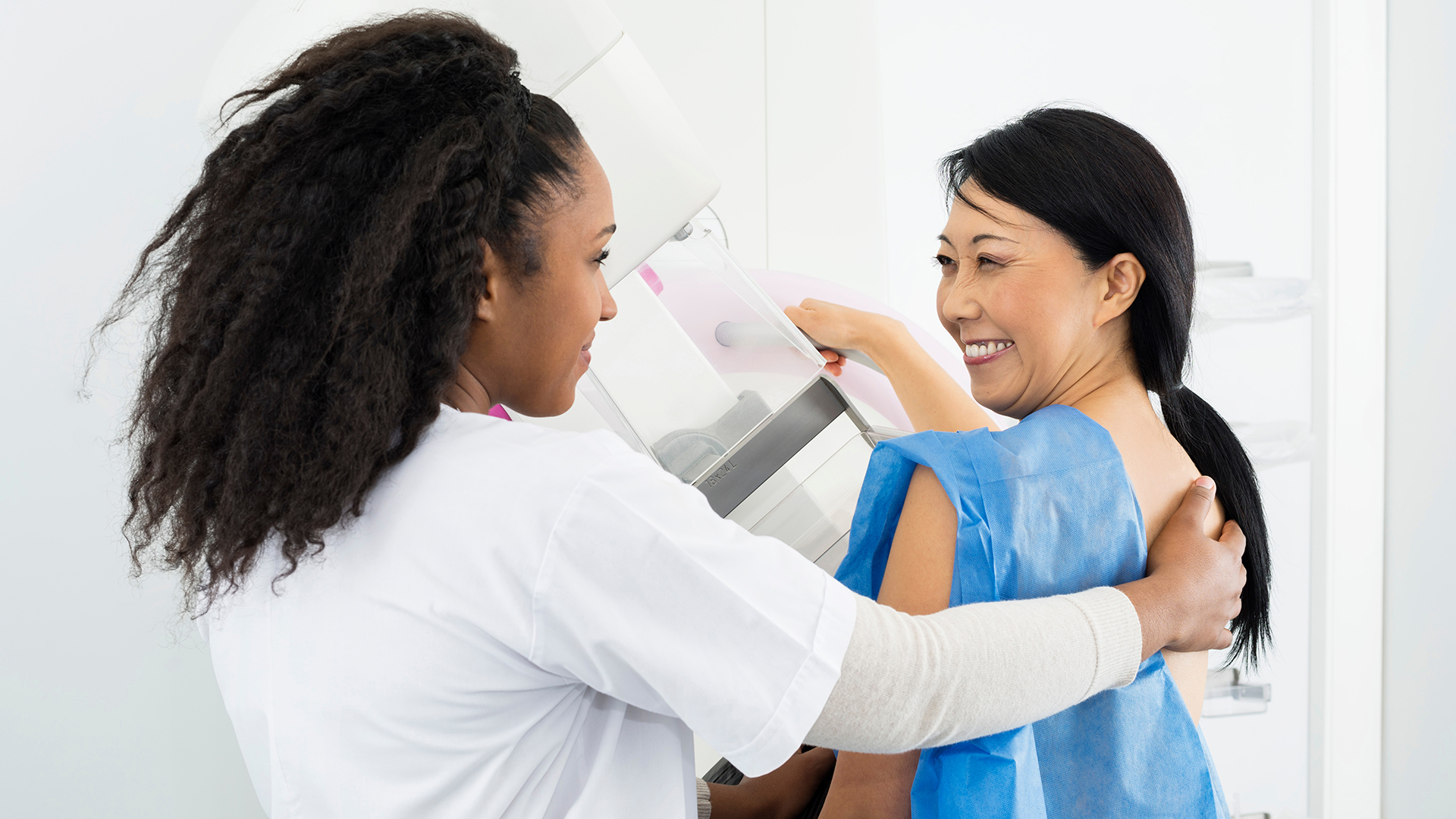 a woman receiving a mammogram smiles at a caregiver