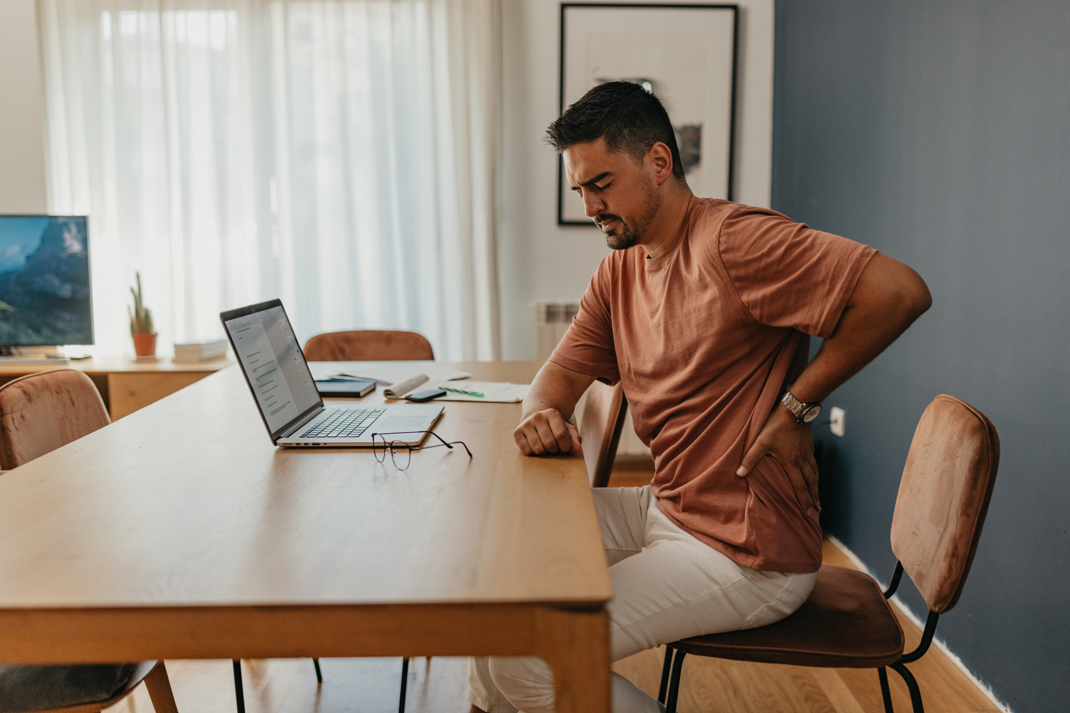 a man sitting at a table holds his lower back in pain