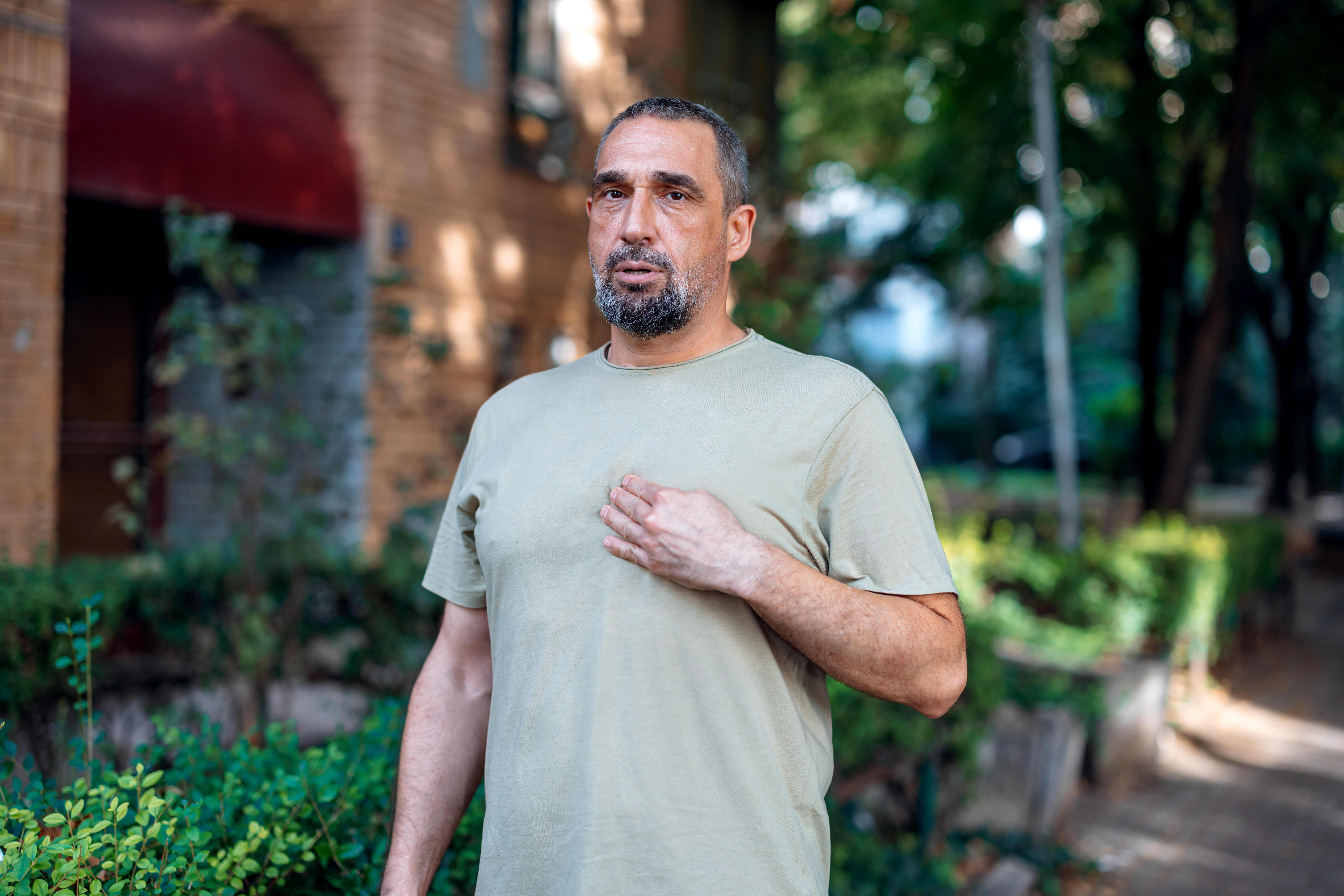 a middle aged man standing outside grabs his chest in pain