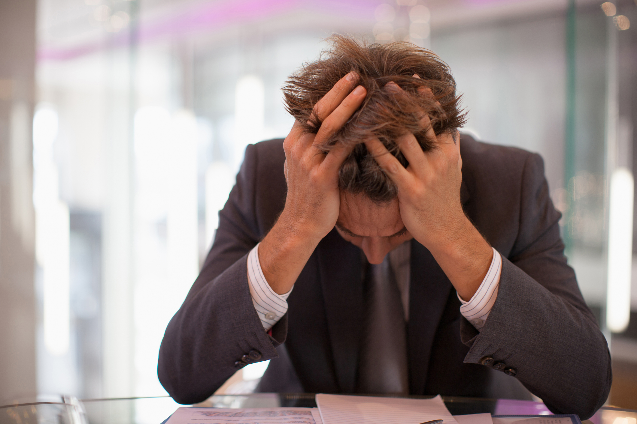A man in a suit holds his head in his hands in distress
