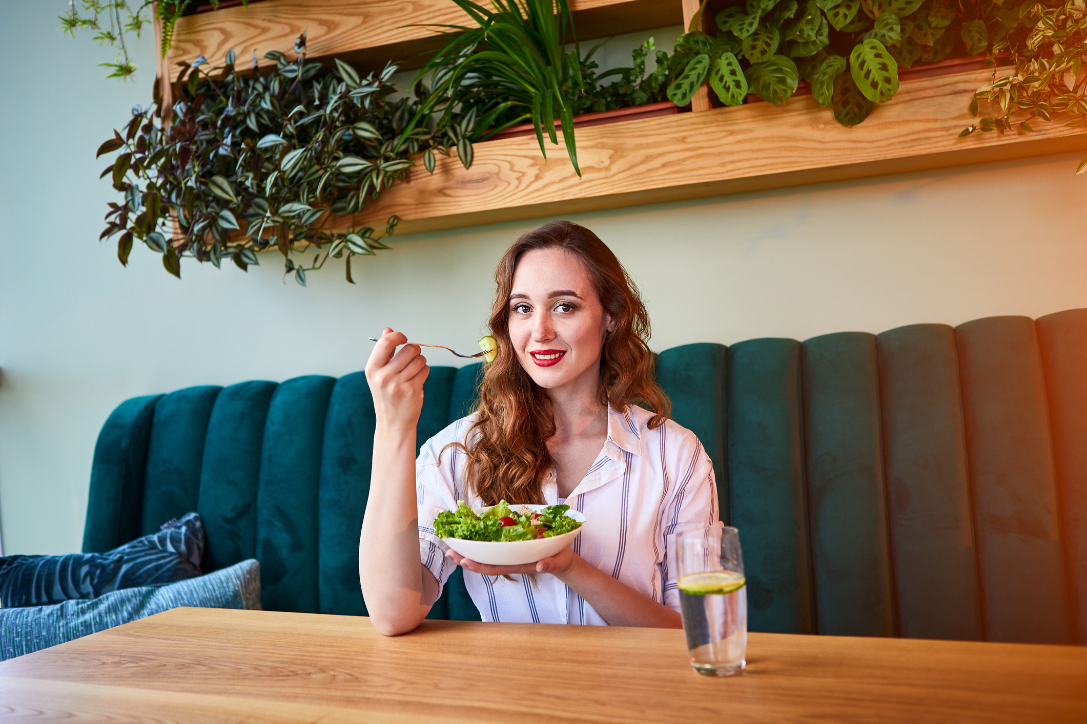 A woman sits at a table holding a salad bowl
