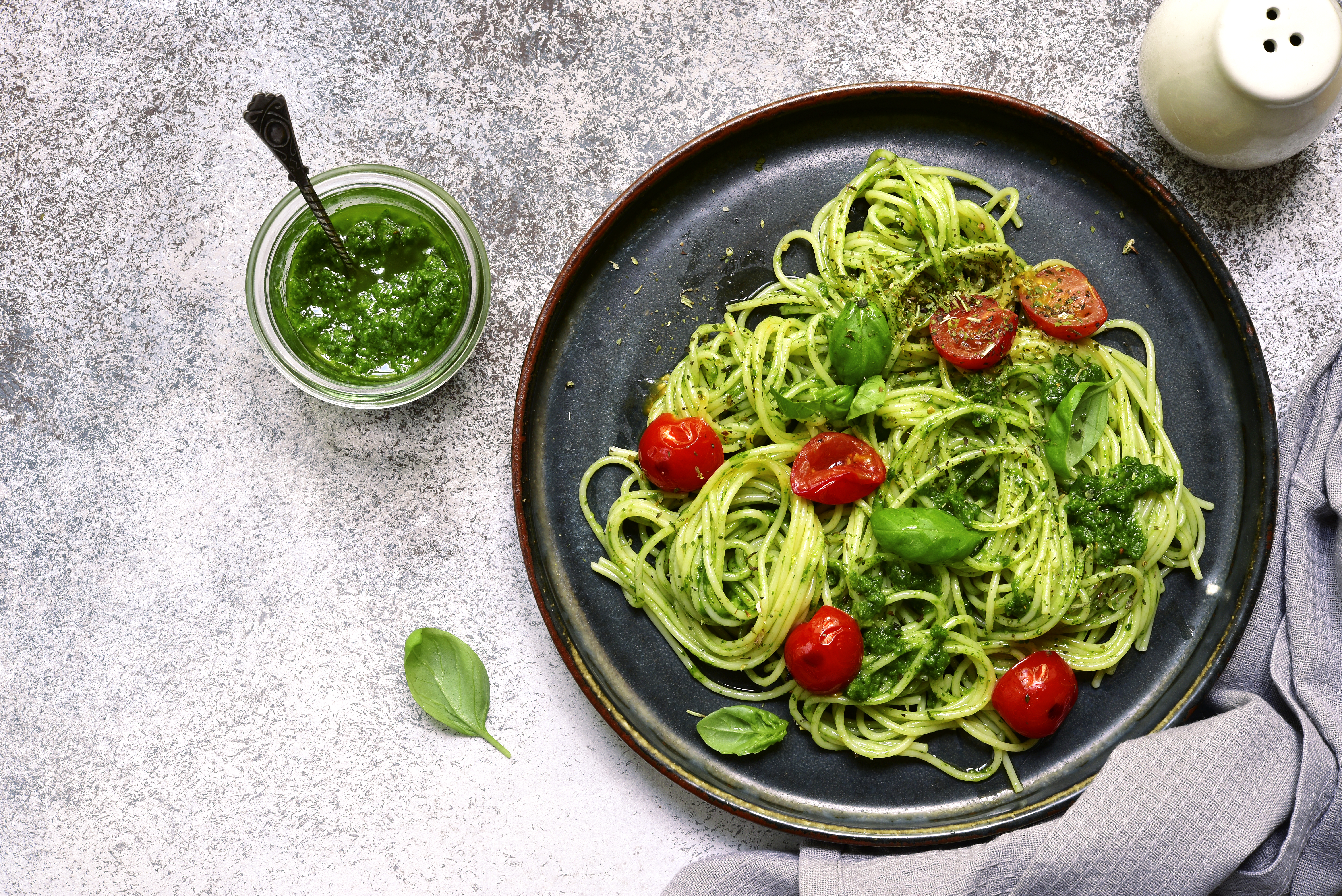Spaghetti pasta with pesto sauce and cherry tomatoes on a plate over light grey slate, stone or concrete background. Top view.