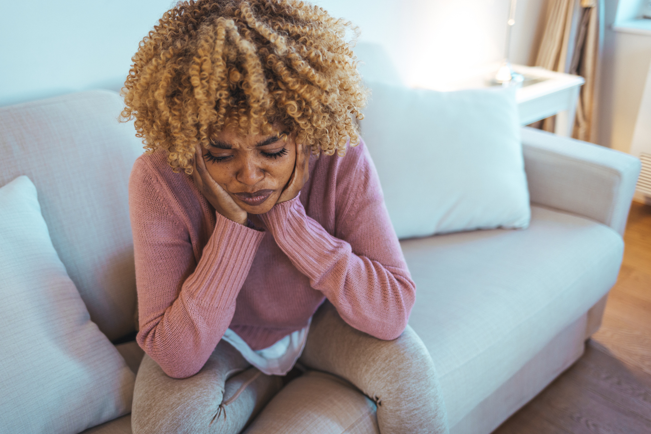 a woman holds her head in pain while sitting on a couch