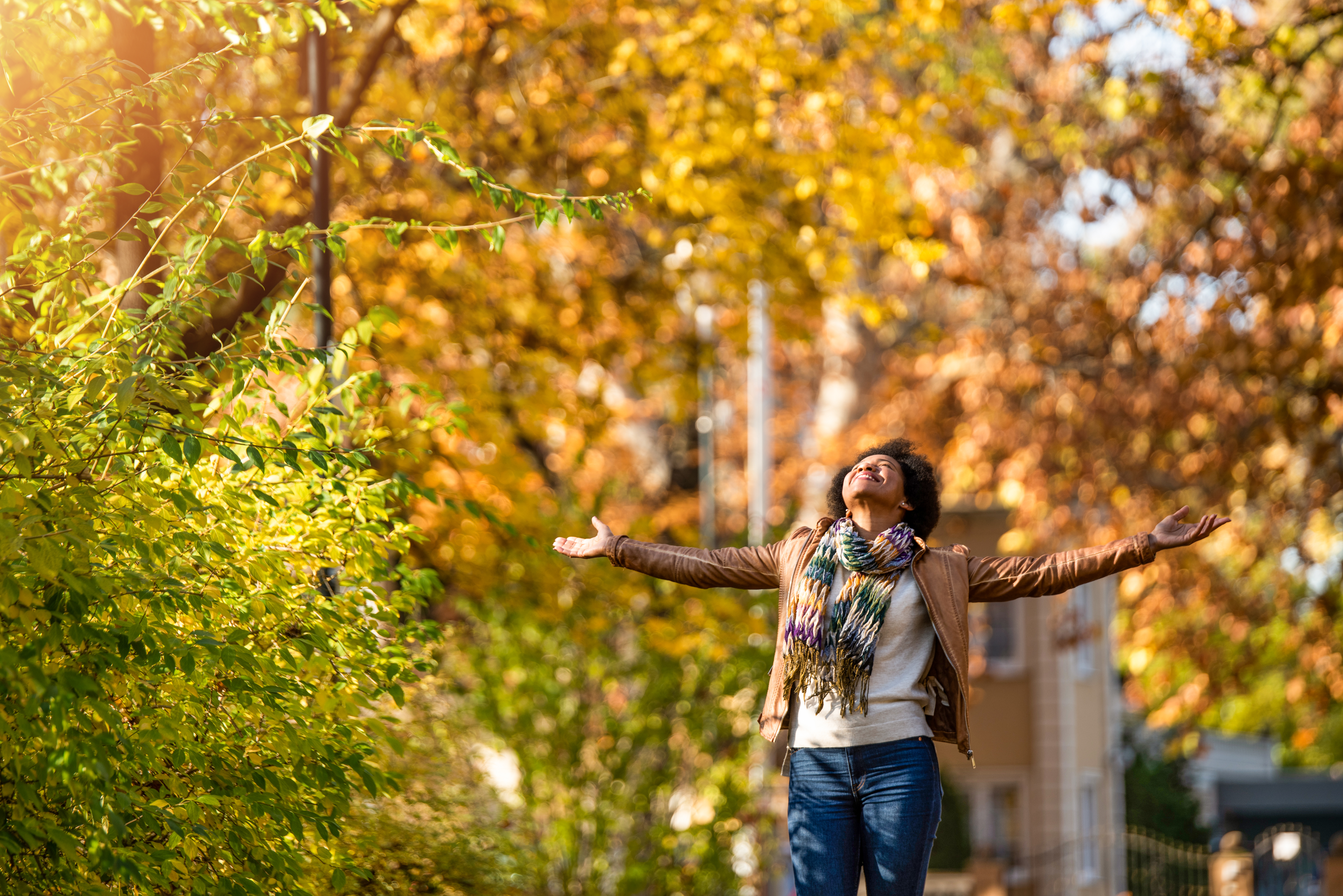 a woman holds her arms open and looks up at the sky and autumn trees