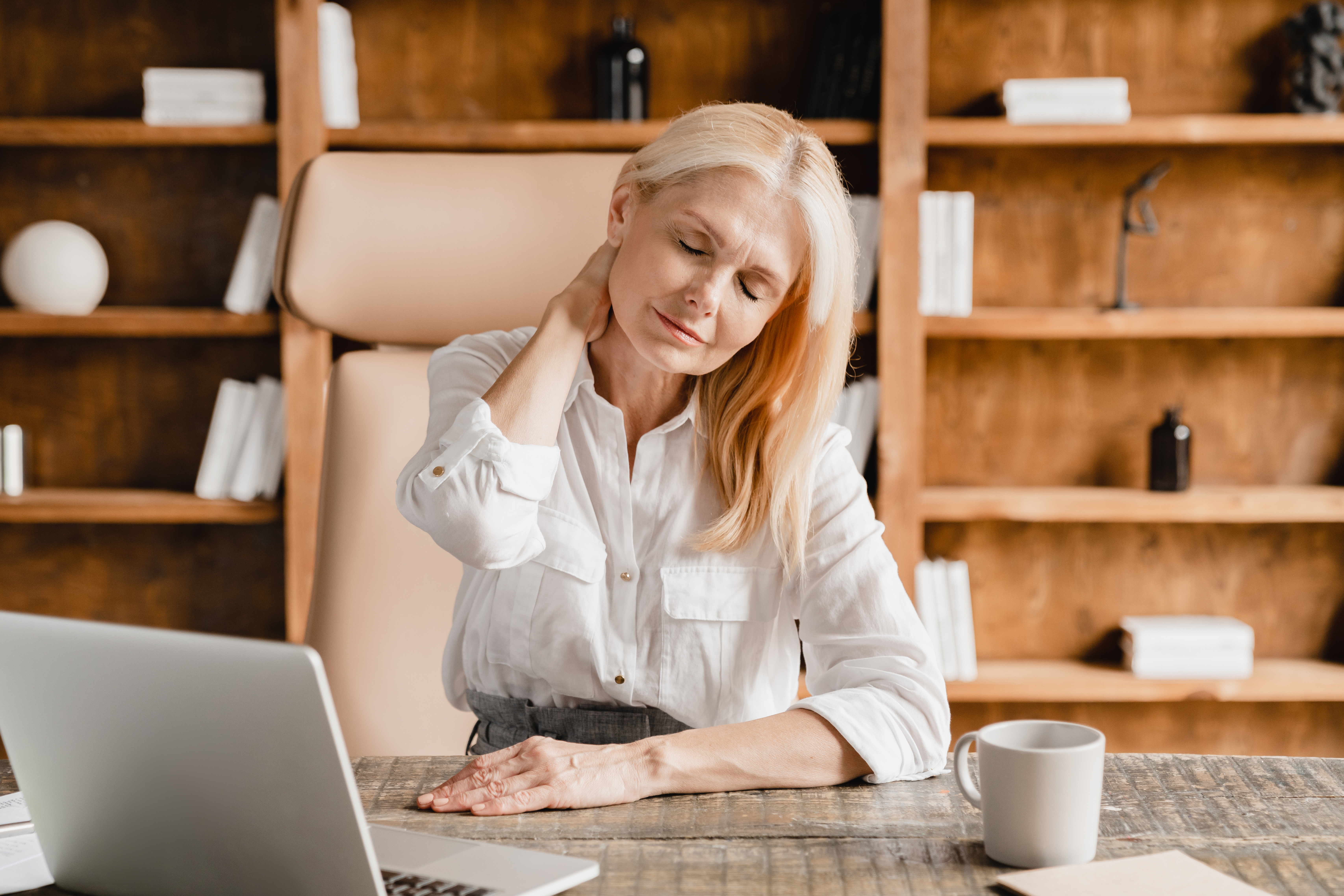 a woman sitting at her work desk grimacing with a headache