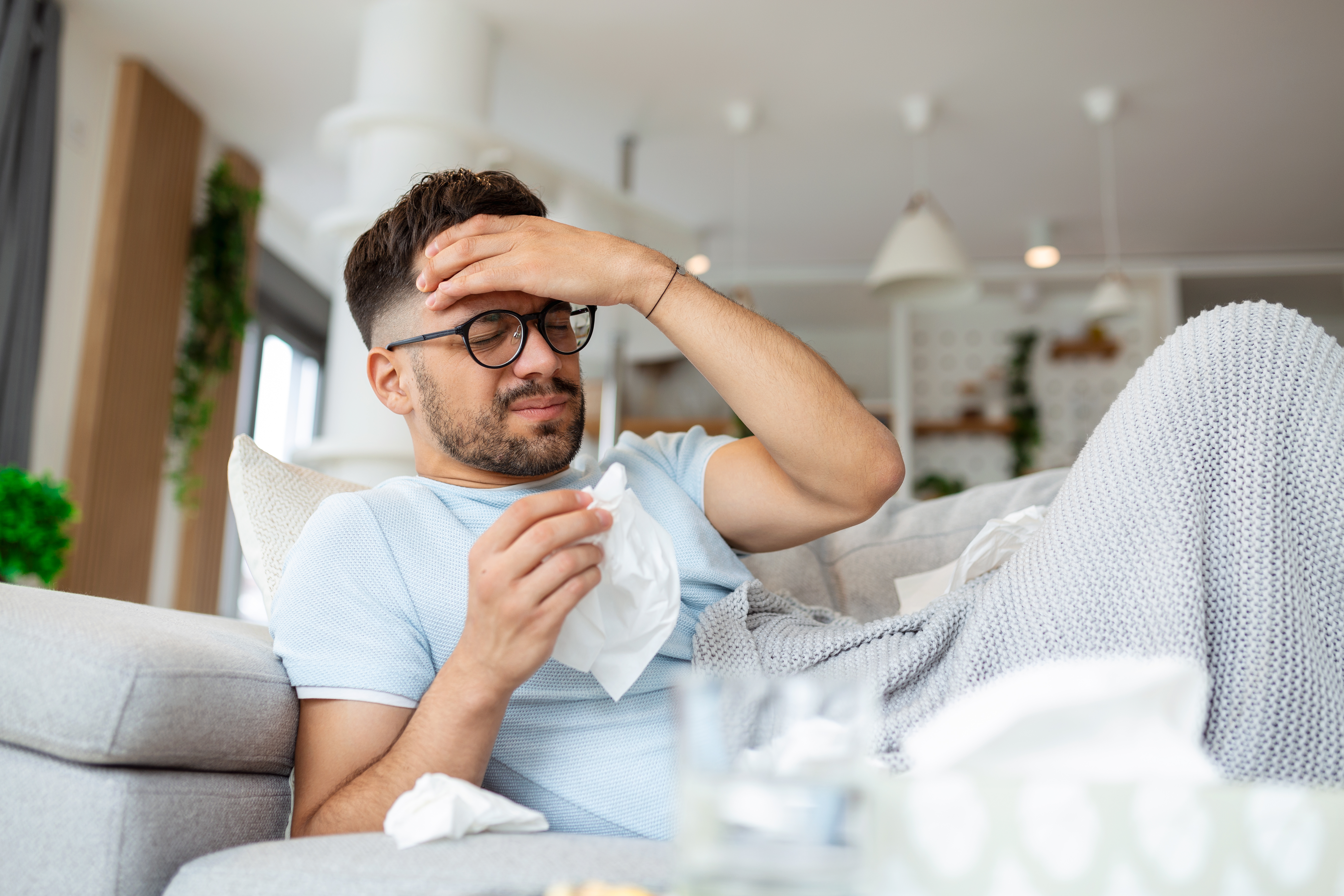 a man sits on his couch holding a tissue and massaging his forehead