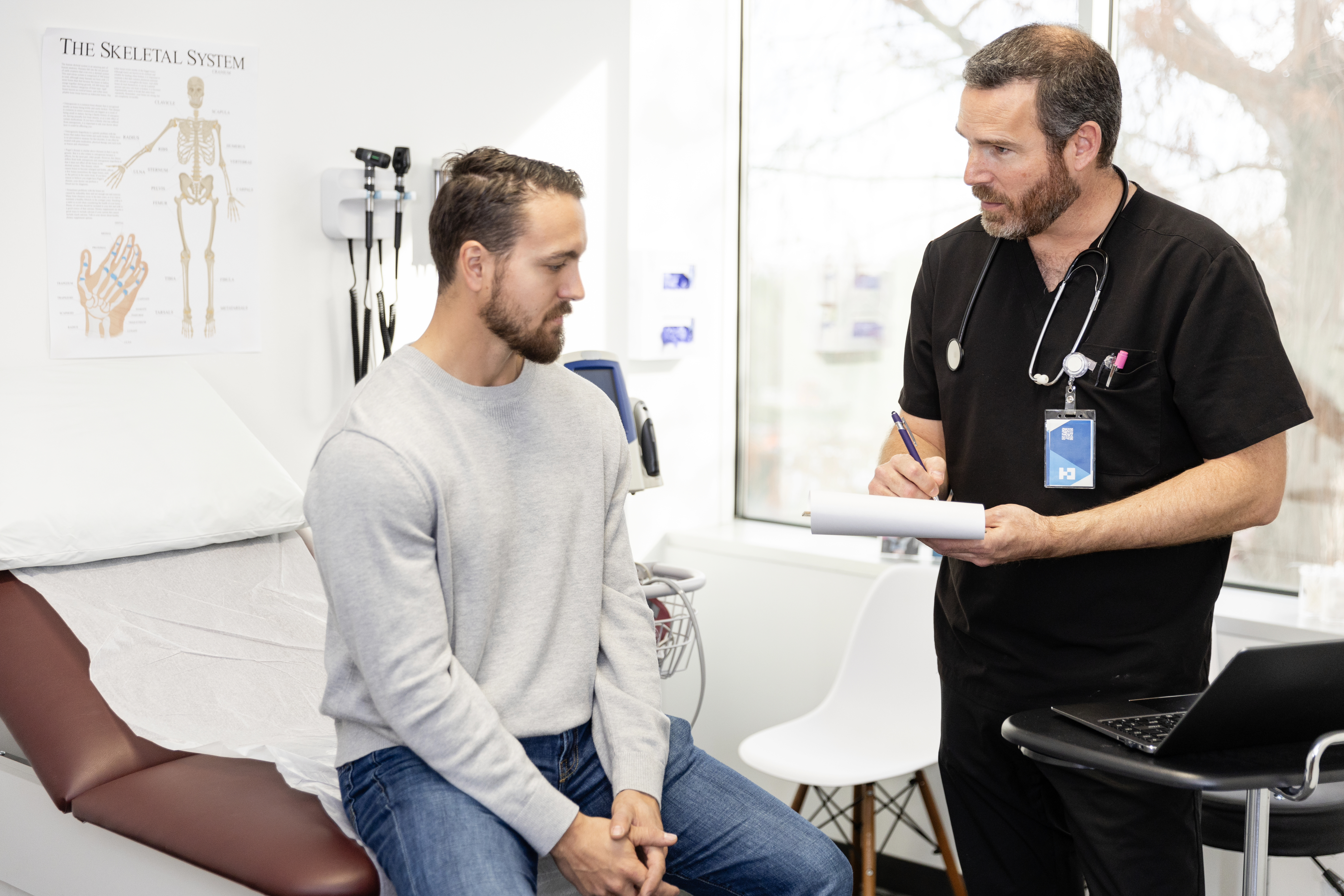 Bearded man speaks to a health care provider in black scrubs and a stethoscope