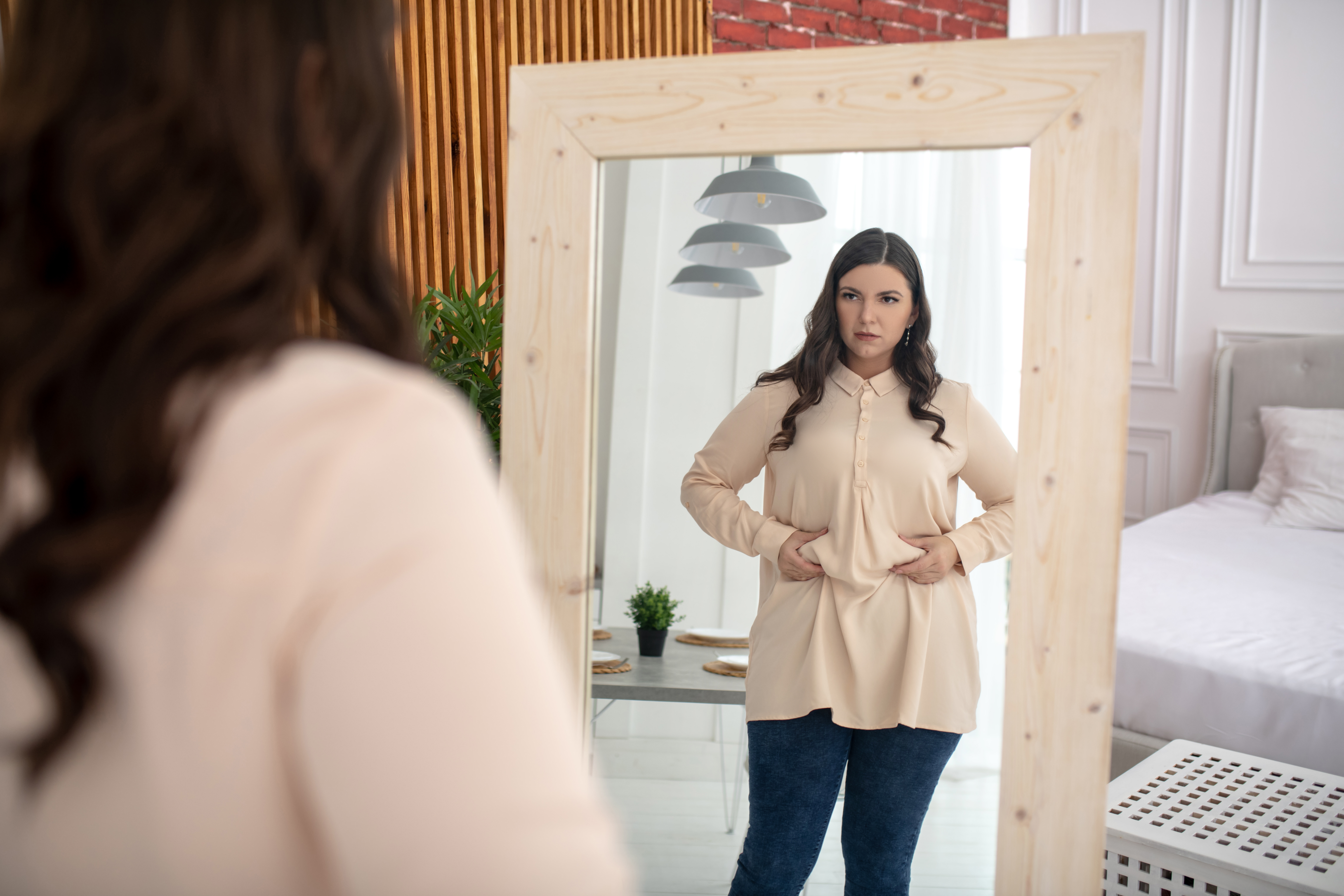 A woman looks at her belly in a mirror