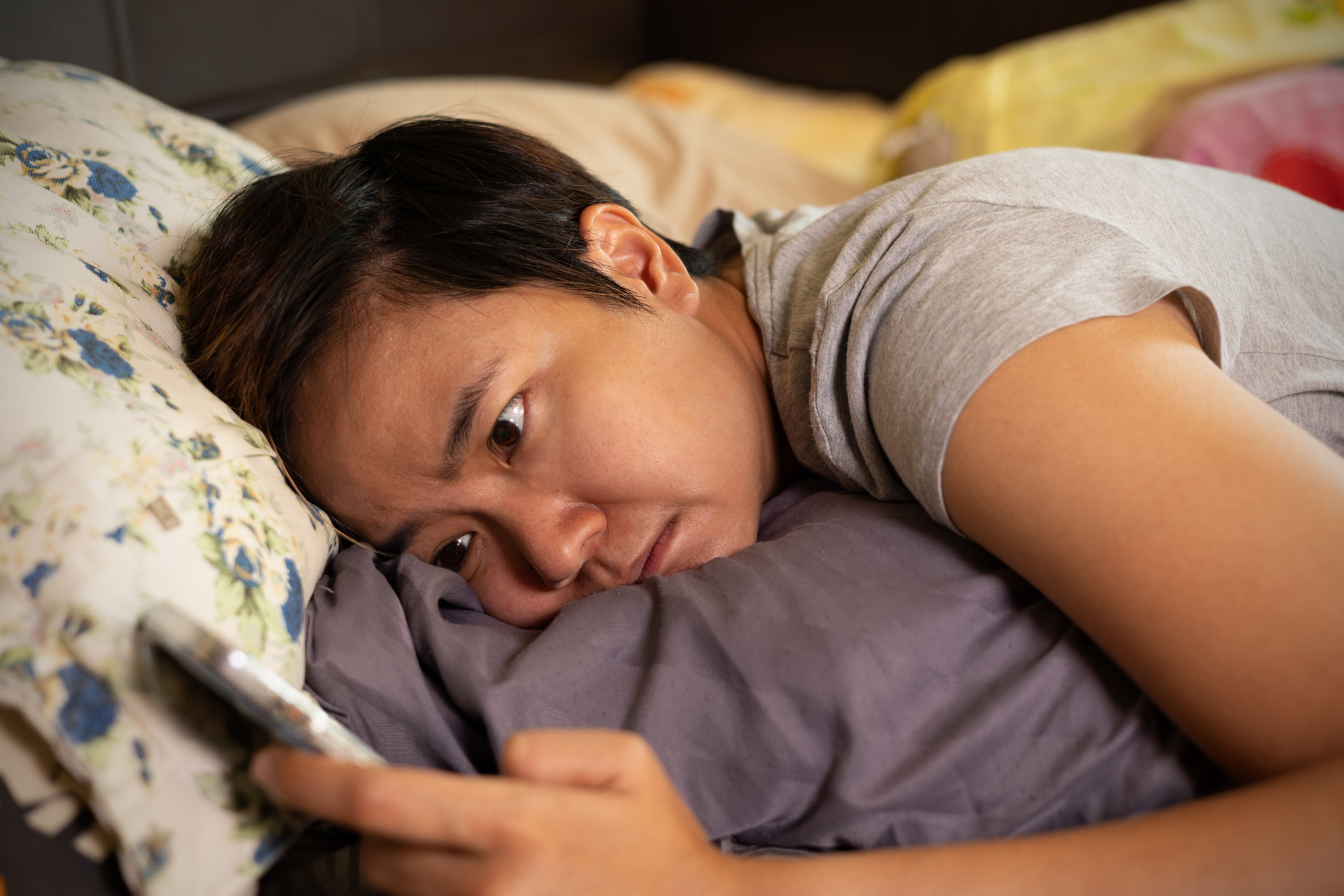 a person struggles to sleep in bed while looking at their phone