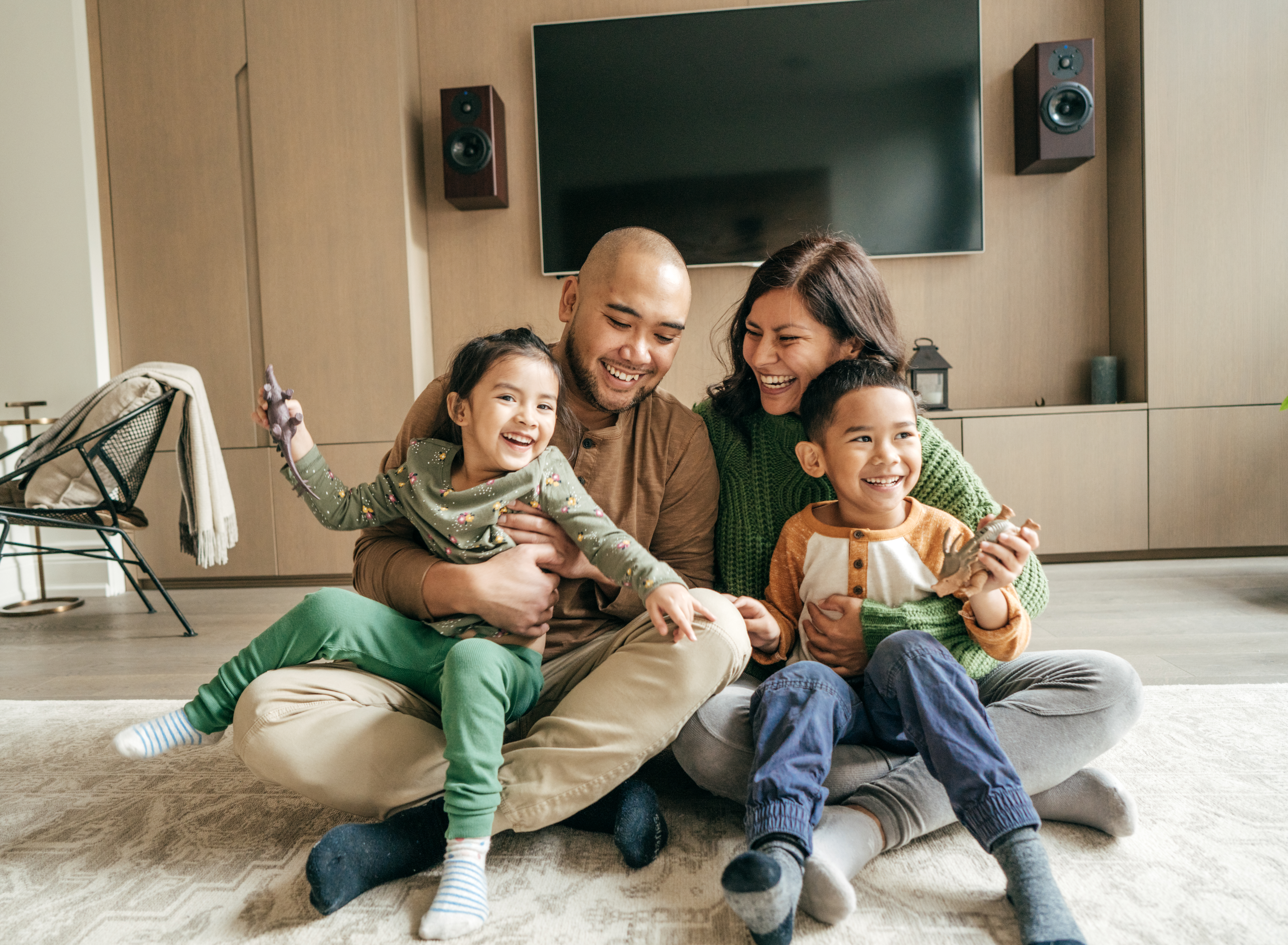 parents with their two children playing and laughing together while sitting on the floor in the living room