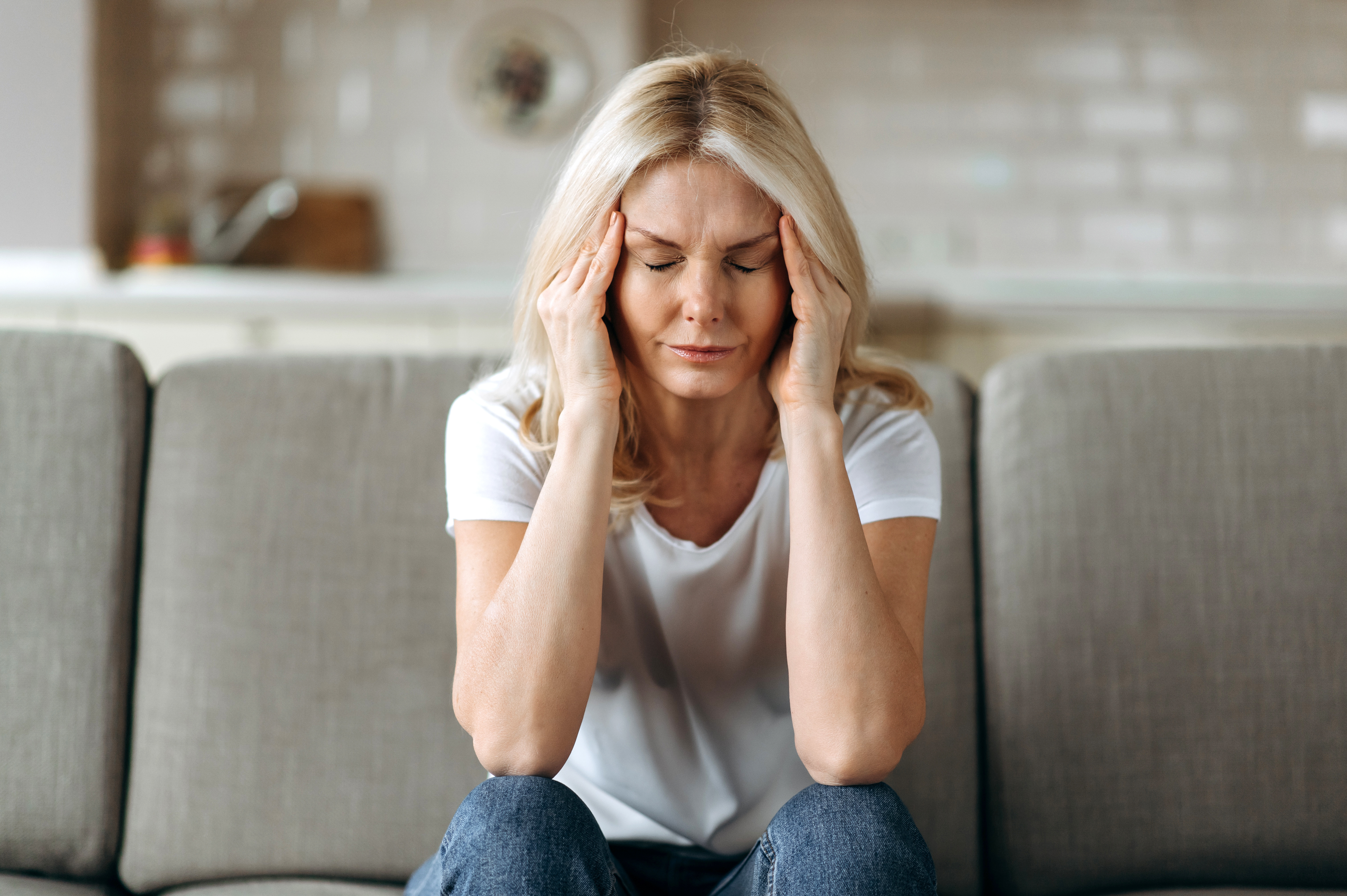 a woman sits on the couch while massing her head in pain