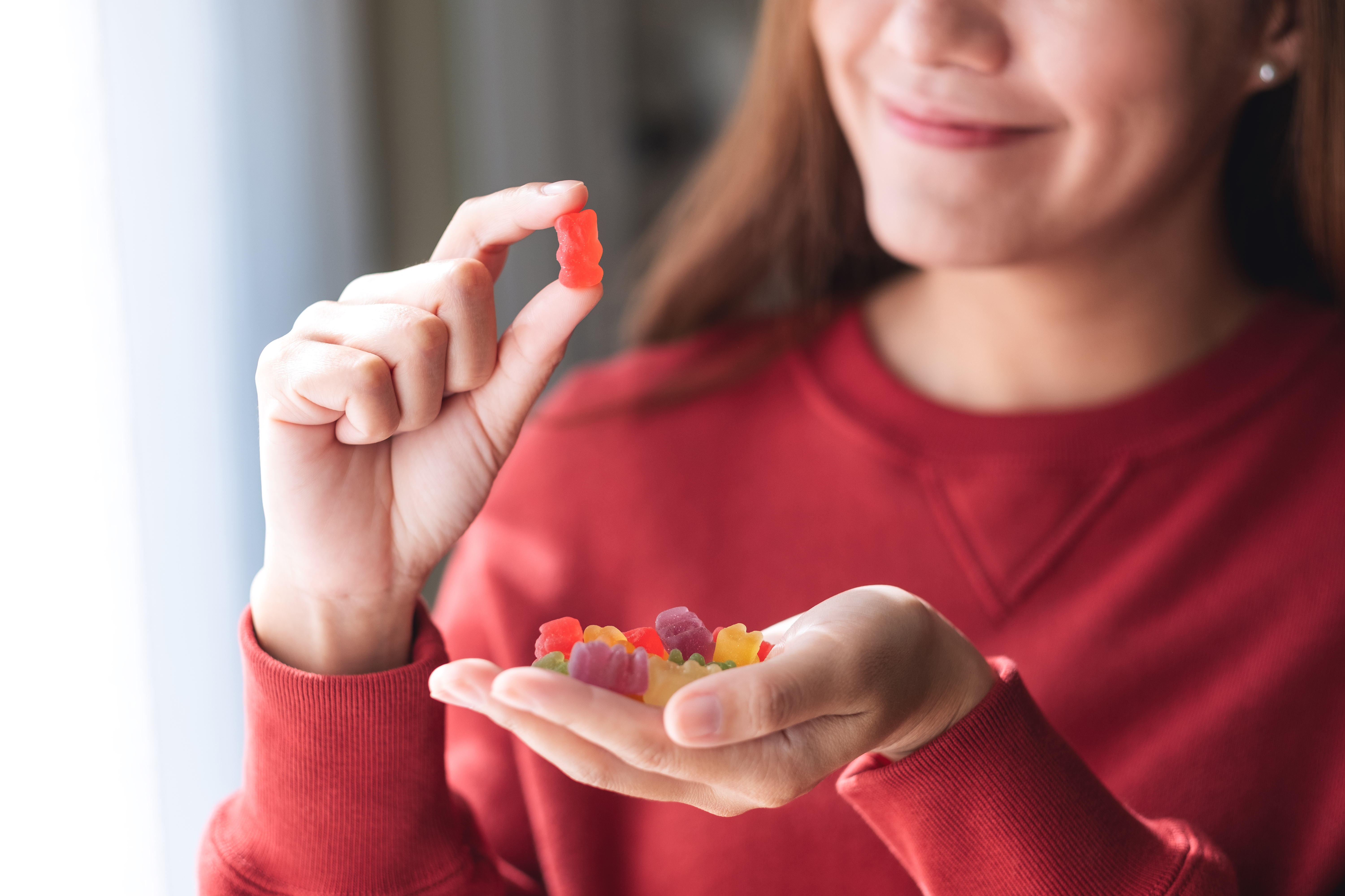 woman in a red sweater with a handful of colorful gummies