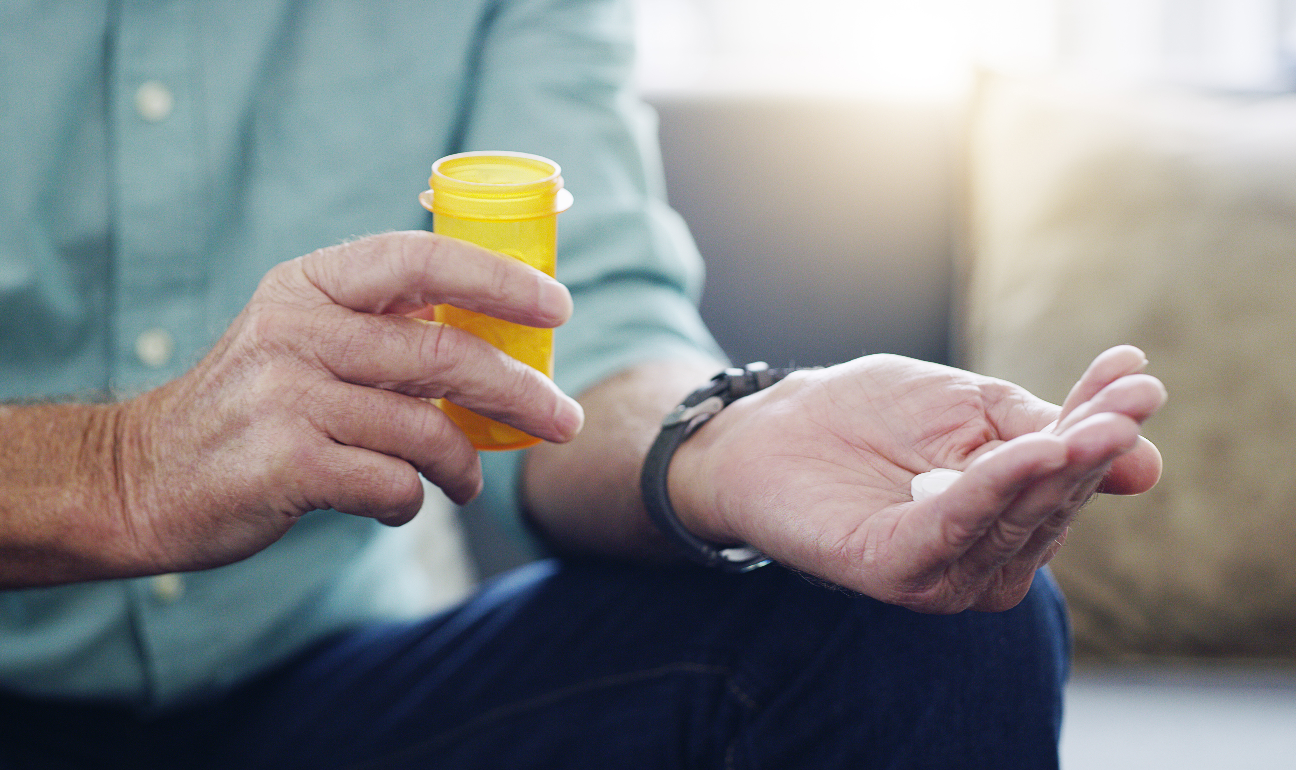 an older man's hands are shown holding a prescription bottle and medicine