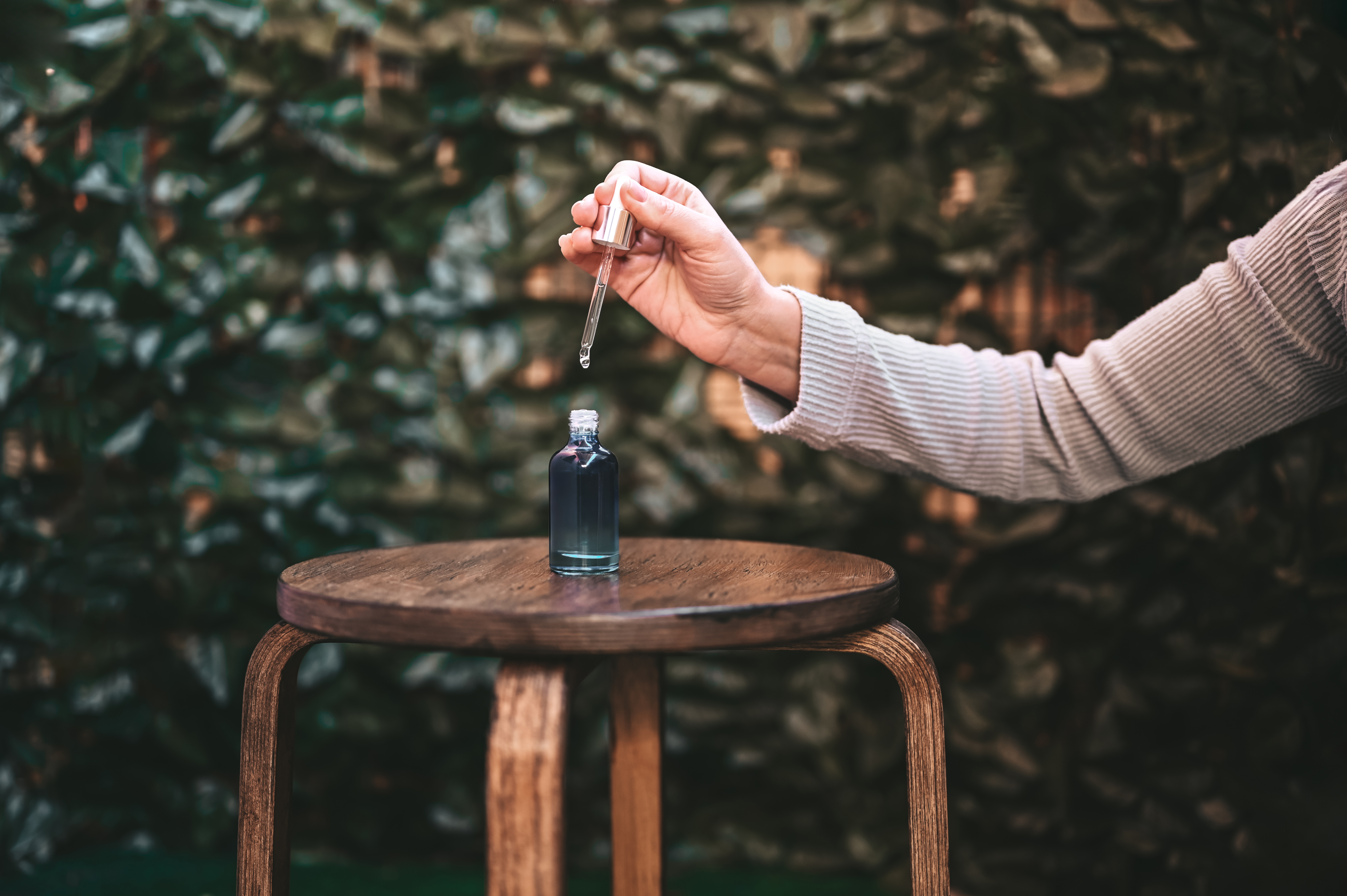 a bottle of peptides is shown sitting on a stool as a hand holds a dropper 