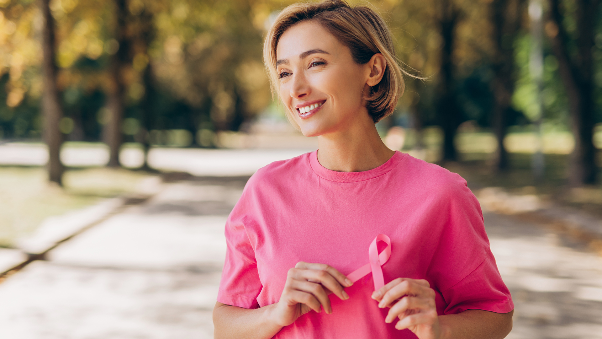a woman wearing pink holds up a pink breast cancer ribbon 