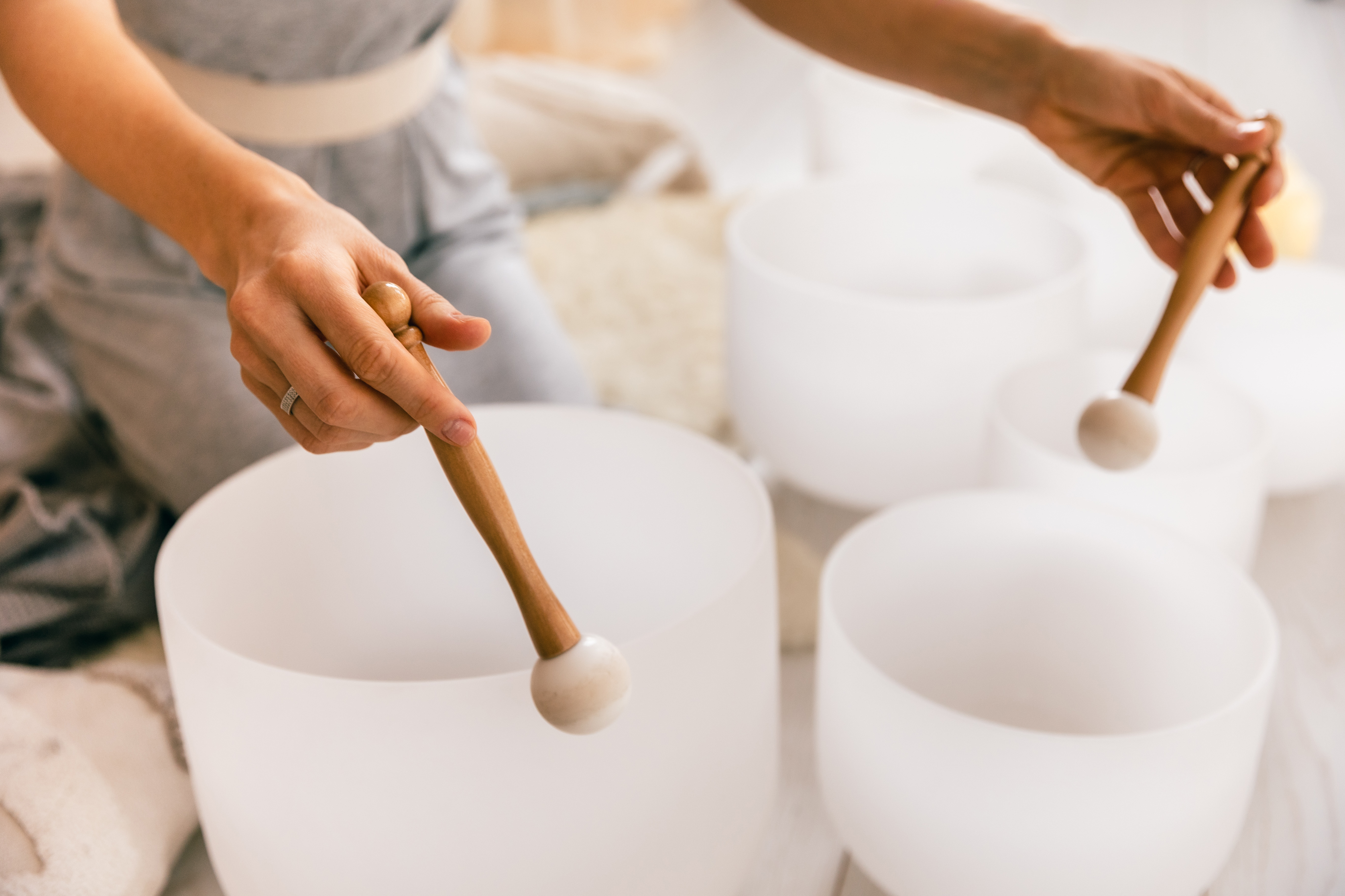 Close-up of hands striking crystal singing bowls with mallets during a sound healing session. Calm wellness atmosphere, mindful music practice, relaxation therapy and positive vibrations.