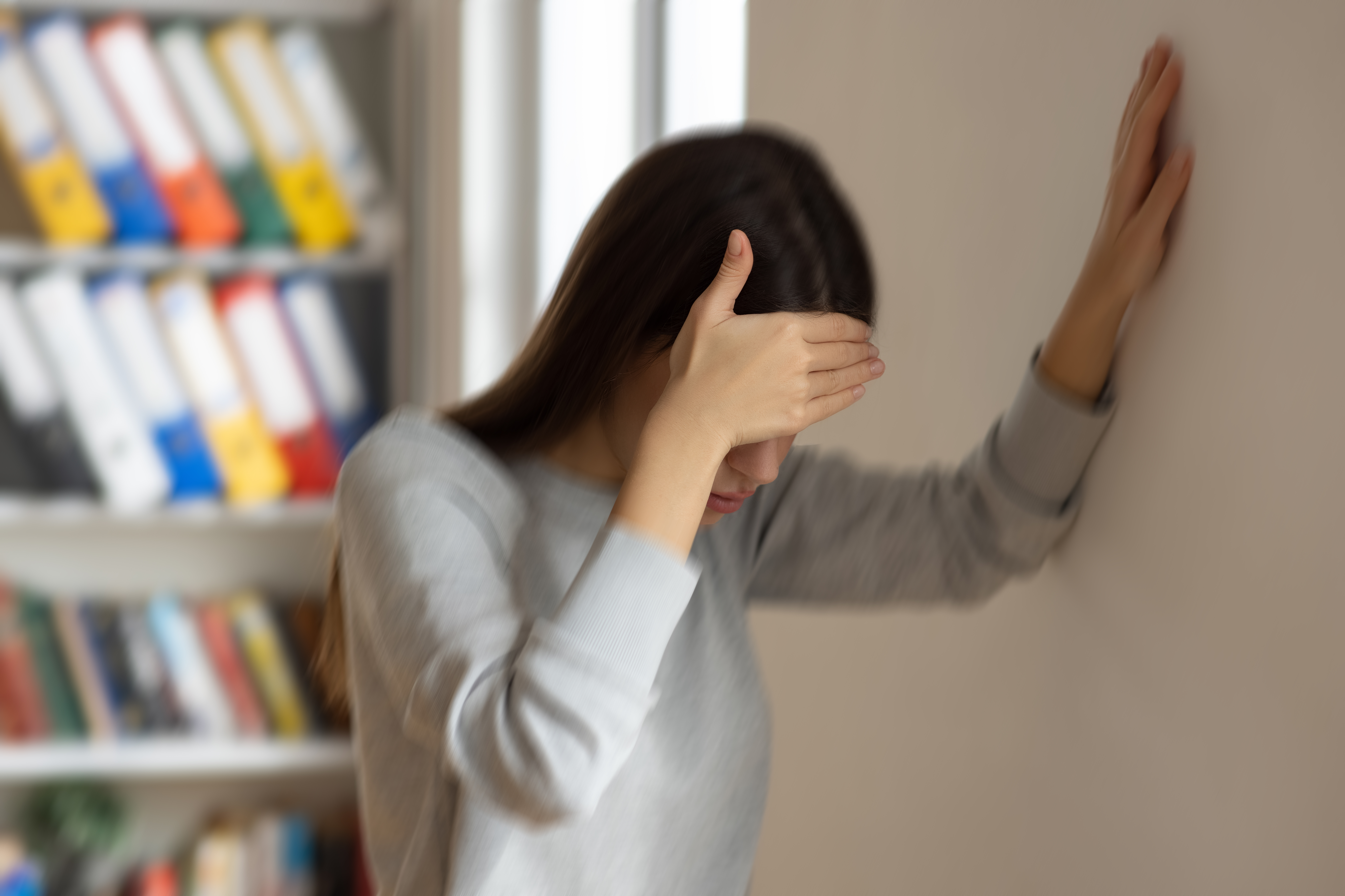 a woman balances herself against a wall as she appears dizzy and in distress